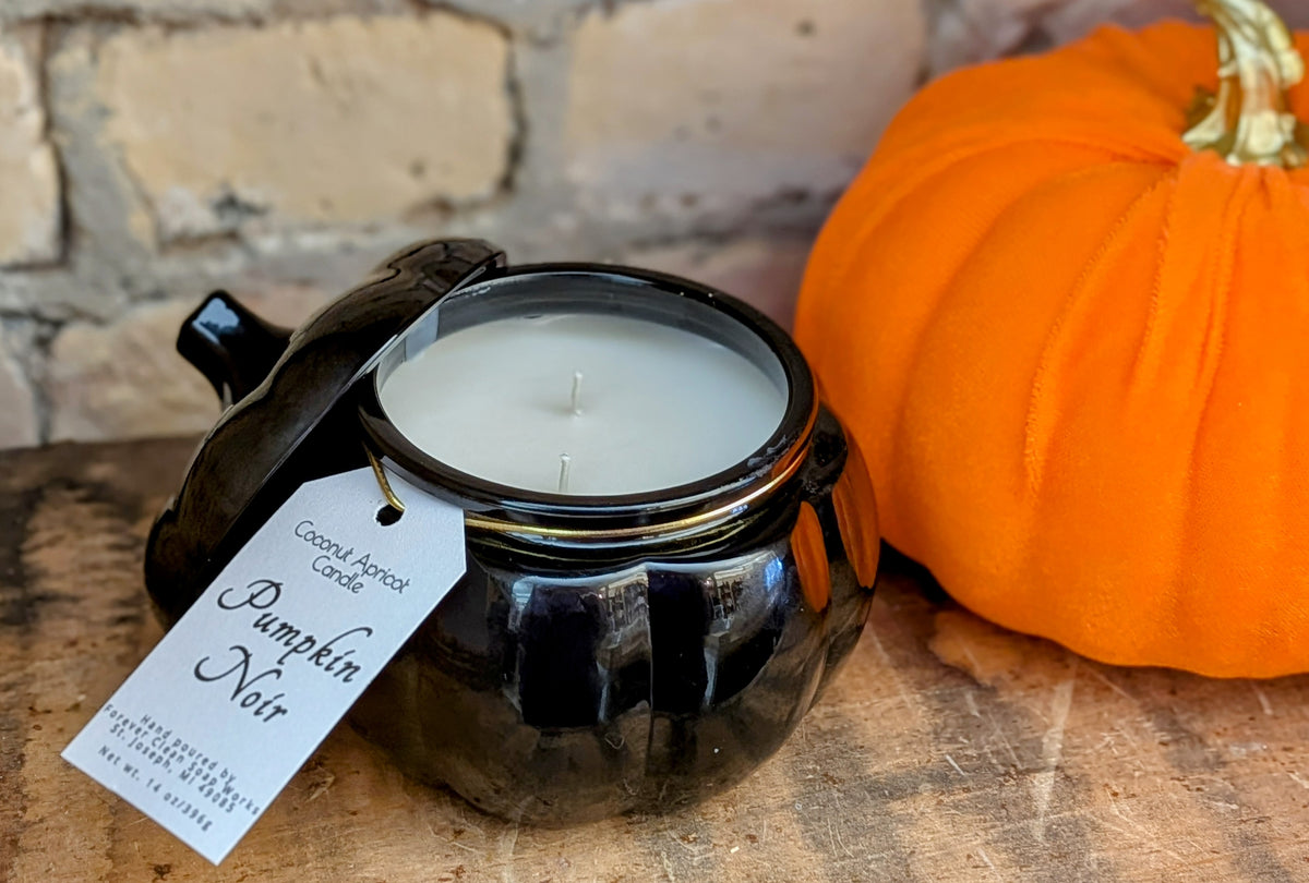 Candle labeled 'Pumpkin jar candle' next to a small pumpkin on a wooden surface with a brick wall background.