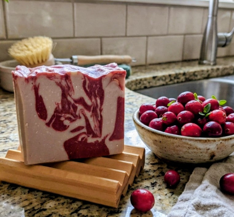 a picture of a bar of cranberry crush soap on a soap deck on a kitchen counter with cranberries surrounding it. 